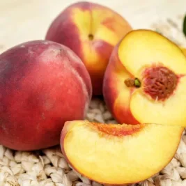 A few peaches, one is sliced open to reveal the juicy insides.