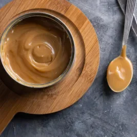 bowl and spoon of melted caramel on wooden potholder