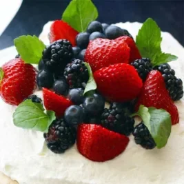 Fresh berries and mint leaves on whipped cream frosting.