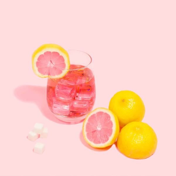 Glass of pink lemonade with lemons surrounding.