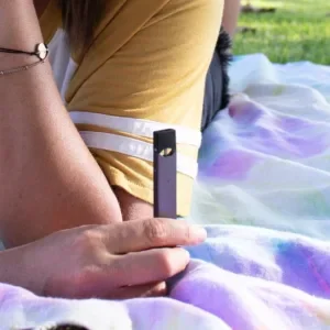 Woman's hand holding a Juul vaping device disposable pod vape outdoors.