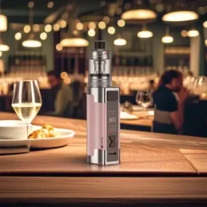 Pink Aspire Zelos 3 vape sitting on a dining table with a glass of white wine and lights in the background.