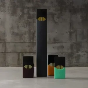 Juul vape with three pods beside it in front of a stark concrete background.